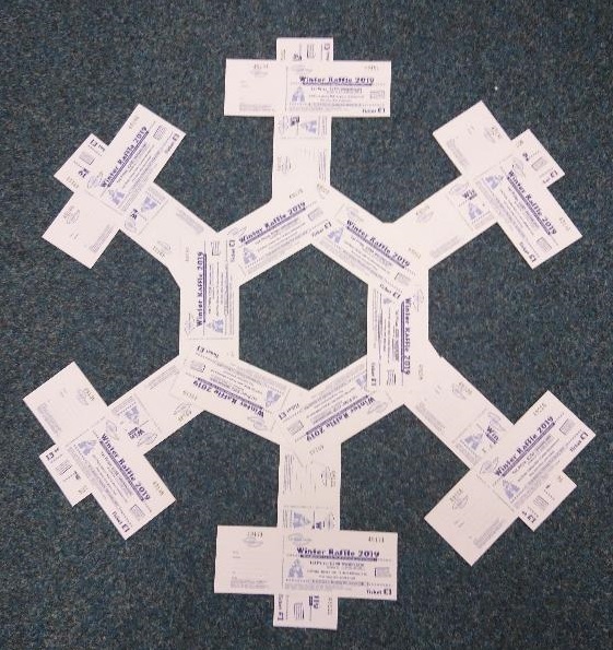 Books of white raffle tickets arranged on a dark background to make a snowflake shape